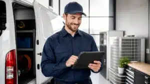 Maintenance technician in a navy uniform uses a tablet beside an open-service van in a workshop.